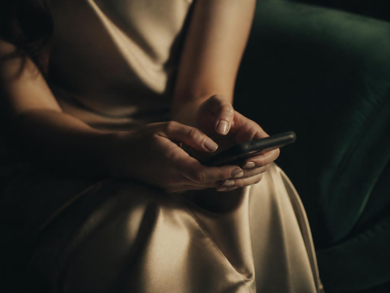 Dłonie kobiety zaciśnięte na telefonie w oczekiwaniu na wiadomość